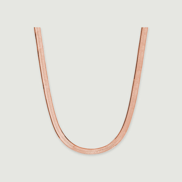 A rose gold herringbone chain displays closely fitted links against a pale gray background.