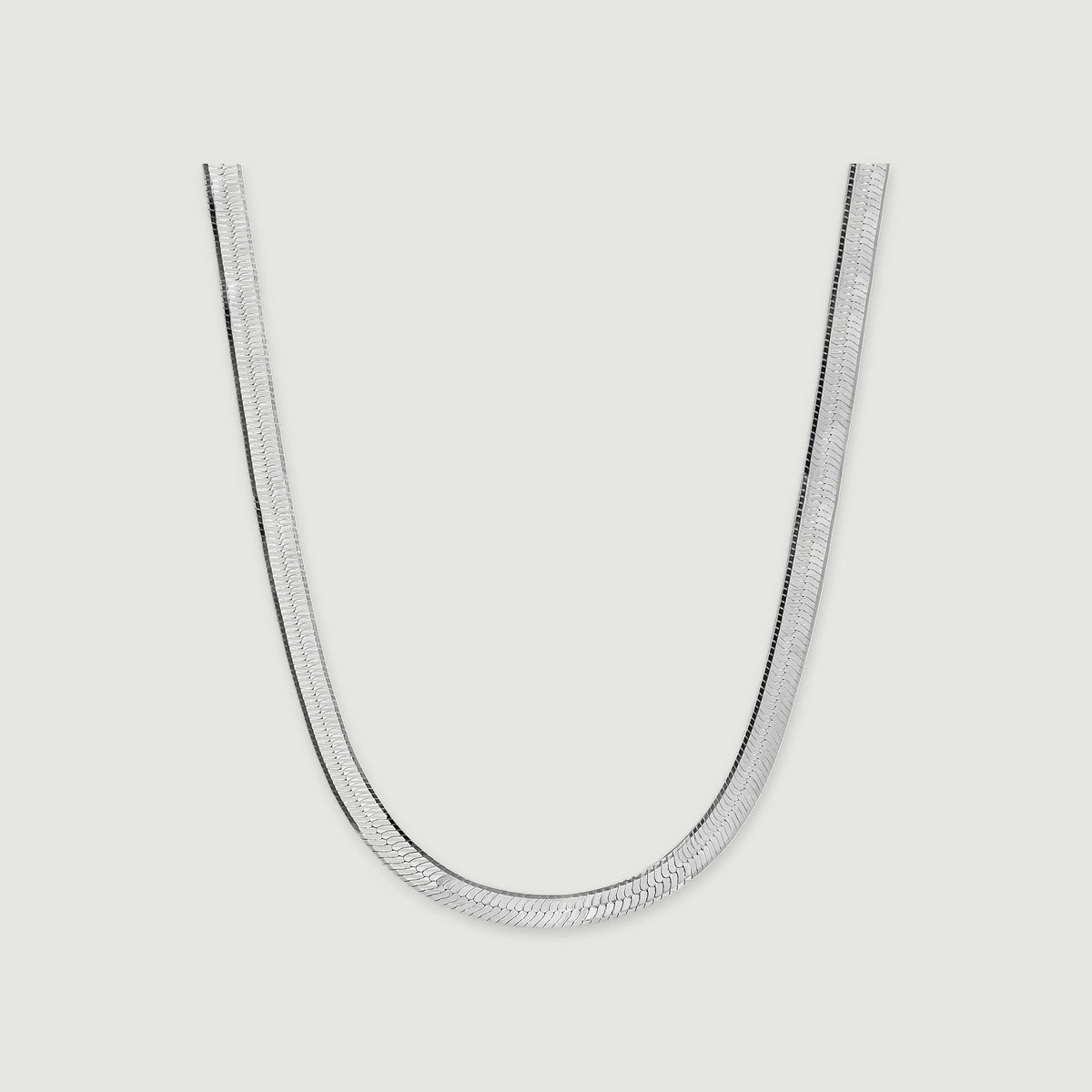 A silver herringbone necklace lies in a broad curve with a soft shadow beneath its edges.