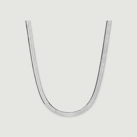 A silver herringbone necklace lies in a broad curve with a soft shadow beneath its edges.