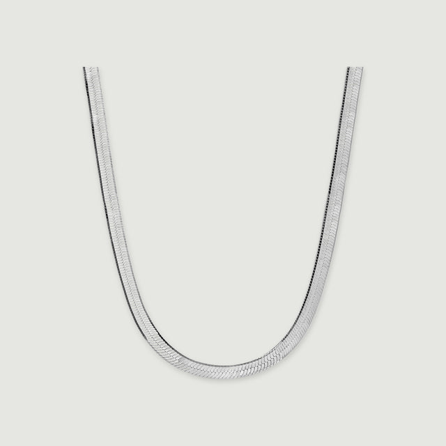 A silver herringbone necklace lies in a broad curve with a soft shadow beneath its edges.