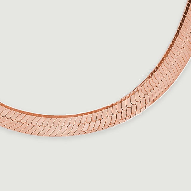 The rose gold necklace bends smoothly across a light gray surface in this close detail.