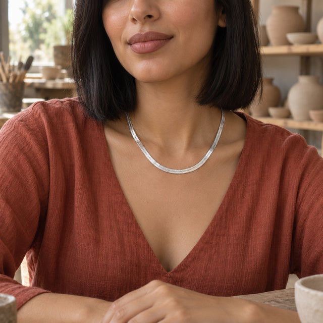A woman in a terracotta shirt wears the silver herringbone necklace at a pottery worktable.