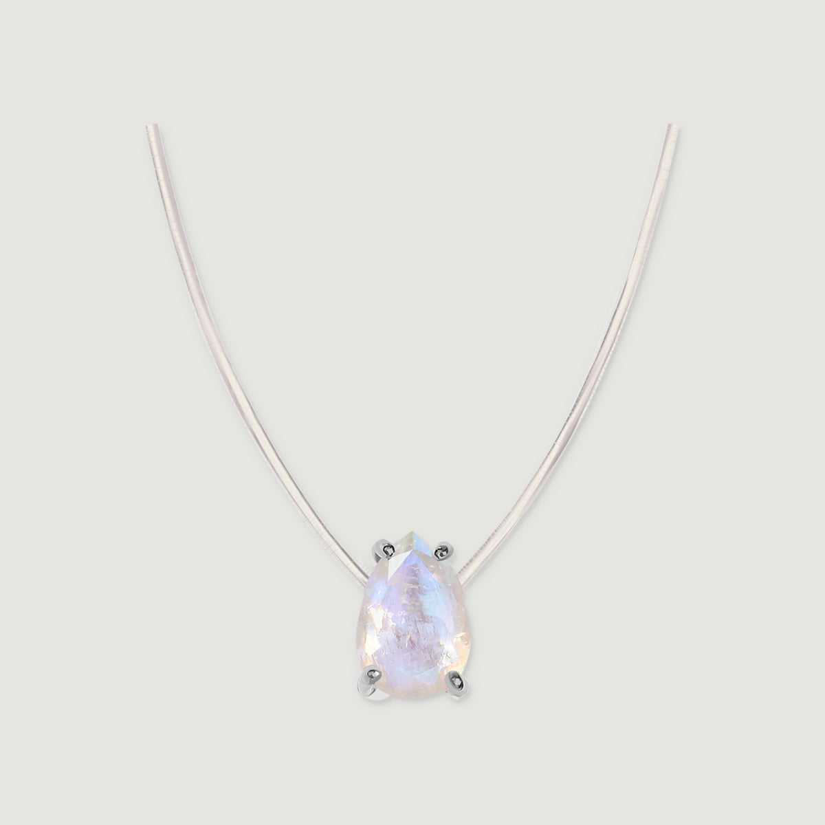 A pear-shaped moonstone in silver prongs hangs from a fine clear cord against a pale gray background.