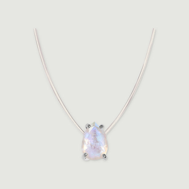 A pear-shaped moonstone in silver prongs hangs from a fine clear cord against a pale gray background.