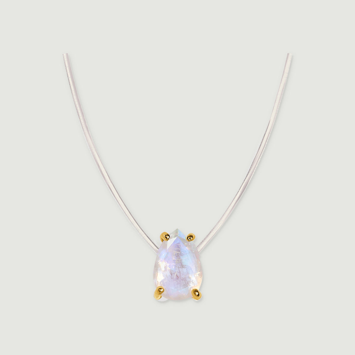 Yellow gold prongs surround a pear-shaped moonstone on a transparent necklace cord over soft gray.