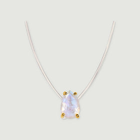 Yellow gold prongs surround a pear-shaped moonstone on a transparent necklace cord over soft gray.