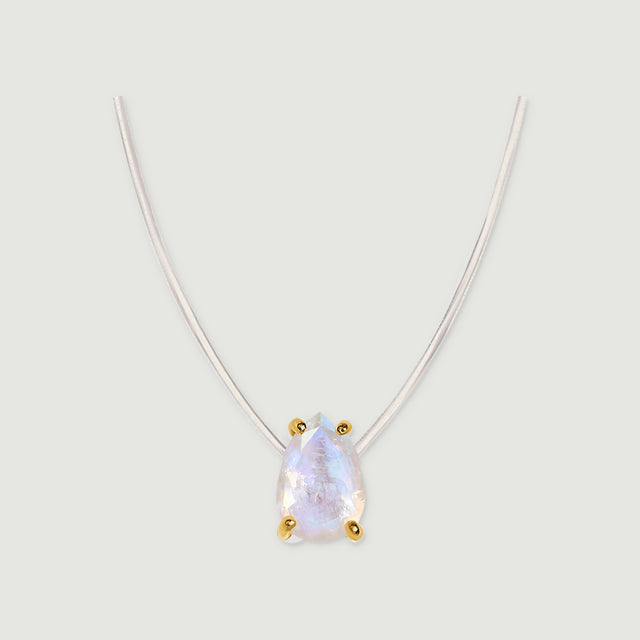 Yellow gold prongs surround a pear-shaped moonstone on a transparent necklace cord over soft gray.