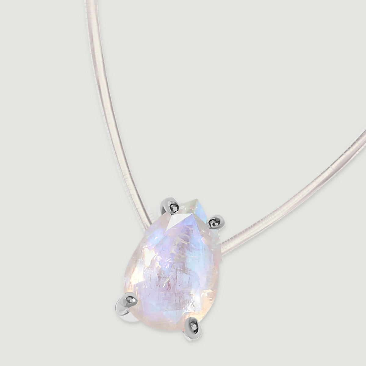 The silver-set pear pendant and two lengths of clear cord lie diagonally across a light gray surface.