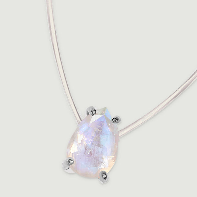 The silver-set pear pendant and two lengths of clear cord lie diagonally across a light gray surface.