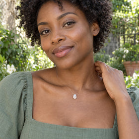 A woman with short curls wears the silver-set moonstone on a clear cord with a sage green top in a leafy garden.