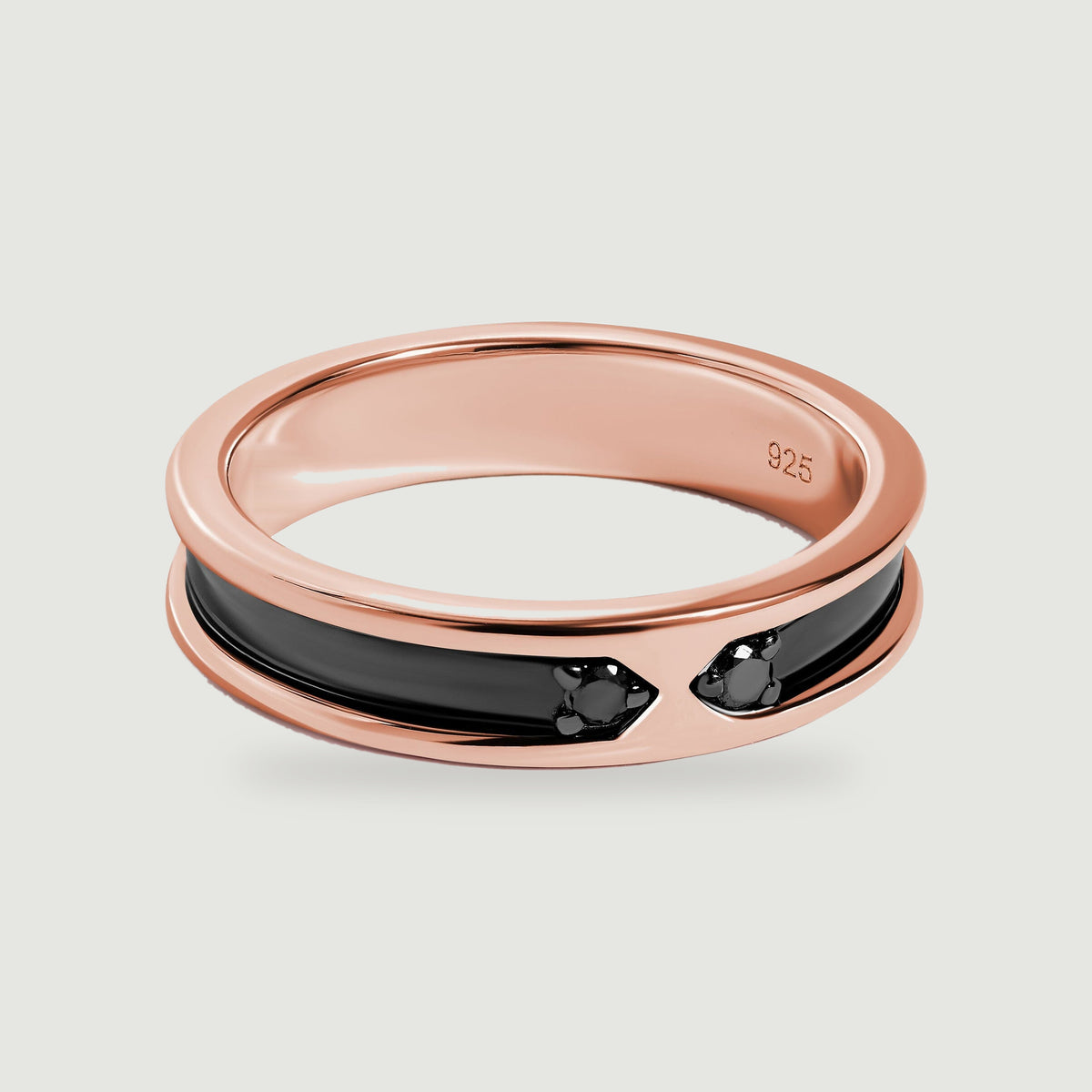 A rose gold ring with a polished black inlay and two small dark stones rests on a light gray surface.
