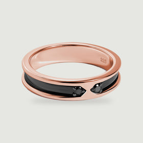 A rose gold ring with a polished black inlay and two small dark stones rests on a light gray surface.