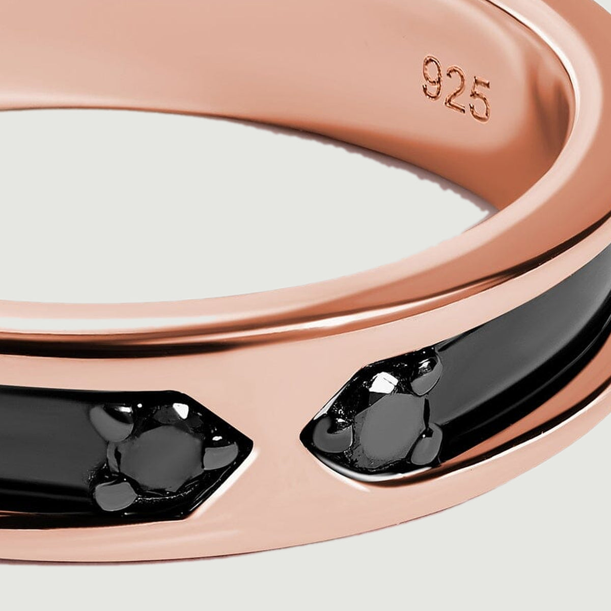 Two small dark stones face each other between polished rose gold edges and a glossy black inlay.