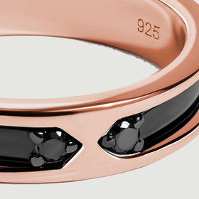 Two small dark stones face each other between polished rose gold edges and a glossy black inlay.