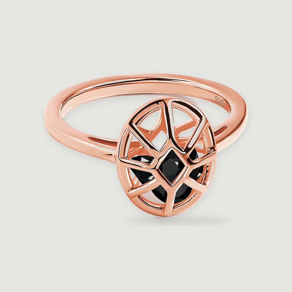 A rose gold ring has an oval openwork cage enclosing three black stones on a pale gray surface.
