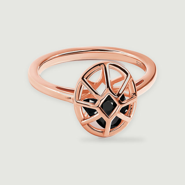 A rose gold ring has an oval openwork cage enclosing three black stones on a pale gray surface.