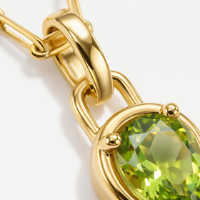 The gold-tone bail and upper prongs frame a bright green faceted peridot in this close-up.