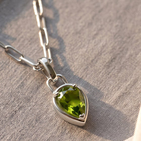 An angled detail reveals the raised silver-tone rim and prongs around the green peridot pendant.