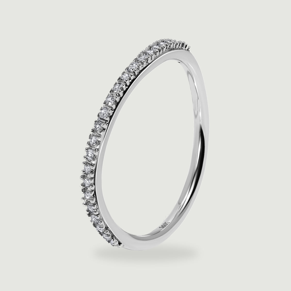 An upright white gold ring shows the side of its round diamond settings above a soft shadow.