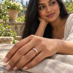 A woman rests her hand on linen at a stone garden table, showing a rose gold band with five round white zircon stones.