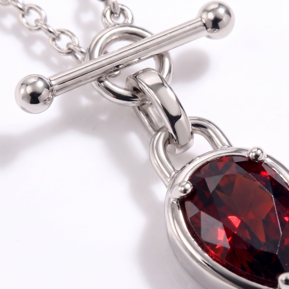 Macro view of the bar clasp, chain links, and faceted deep-red pear gemstone pendant.