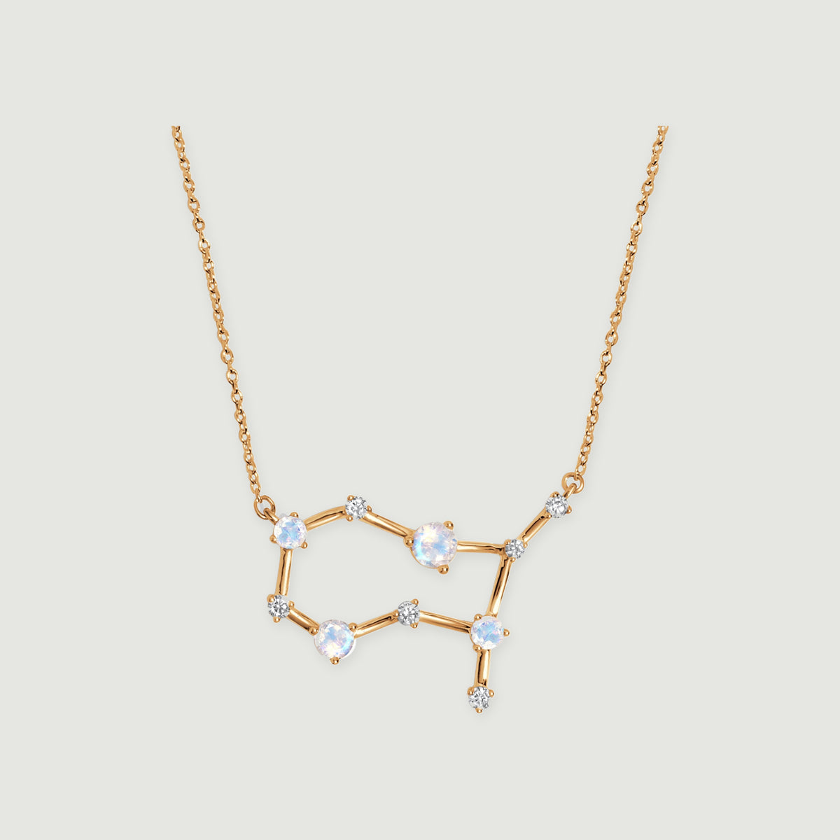 A yellow gold constellation necklace with four pale moonstones and small clear stones rests on a light gray background.