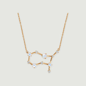 A yellow gold constellation necklace with four pale moonstones and small clear stones rests on a light gray background.