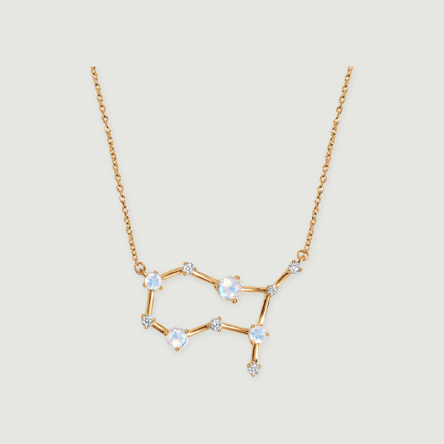 A yellow gold constellation necklace with four pale moonstones and small clear stones rests on a light gray background.
