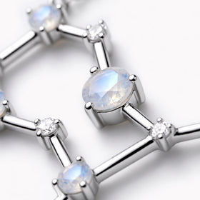 A faceted pale blue moonstone sits in a silver prong setting between polished bars and small round clear stones.