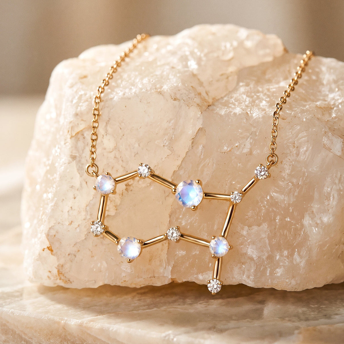 A yellow gold constellation pendant and its link chain are arranged over a pale textured stone on a clean tabletop.