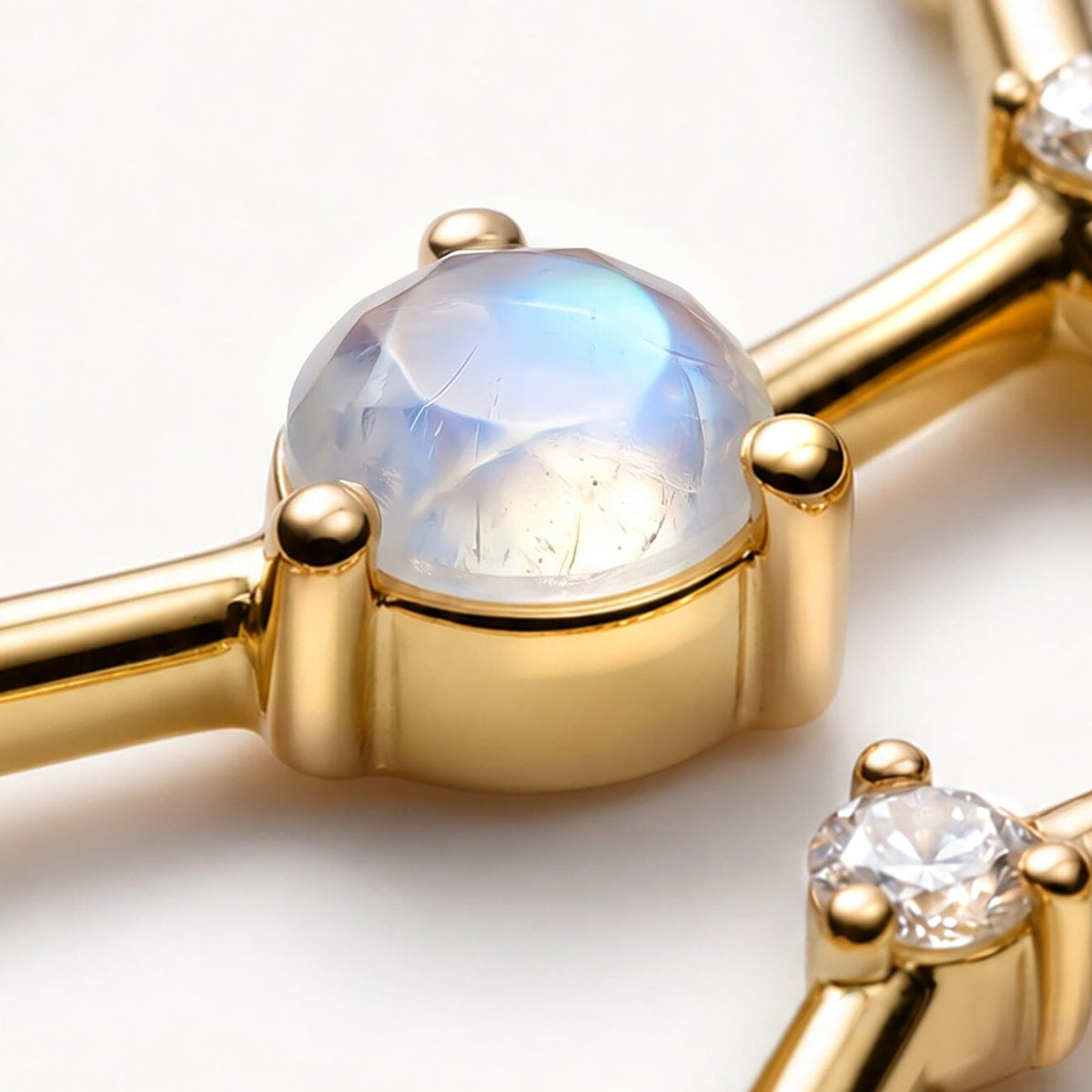 An angled close-up shows the raised yellow gold cup and rounded prongs beneath a blue-sheened moonstone.