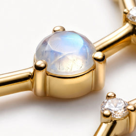 An angled close-up shows the raised yellow gold cup and rounded prongs beneath a blue-sheened moonstone.