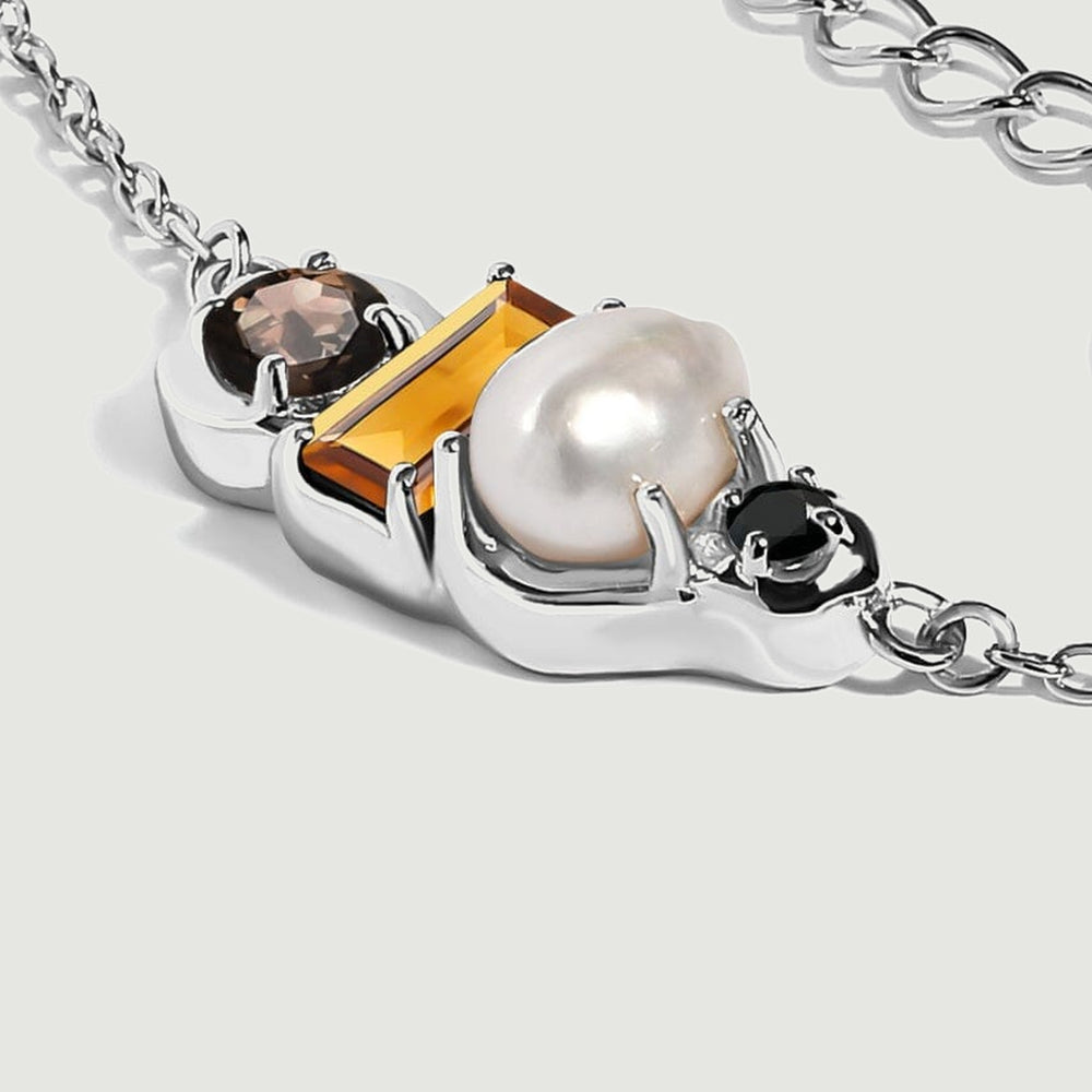 An angled close-up shows the silver setting beneath the pearl and amber citrine with round dark stones at either end.