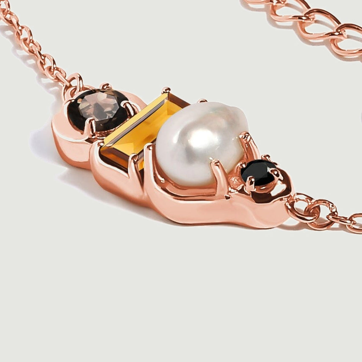 A rose gold vermeil pendant is seen at an angle, showing the raised pearl and the depth of its polished stone settings.