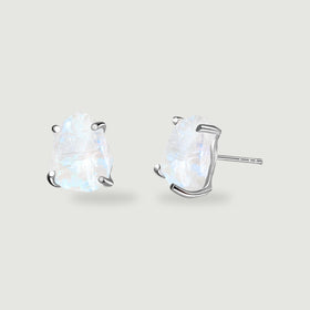 Two raw moonstone studs with silver prongs rest on a light gray surface, with one post visible.
