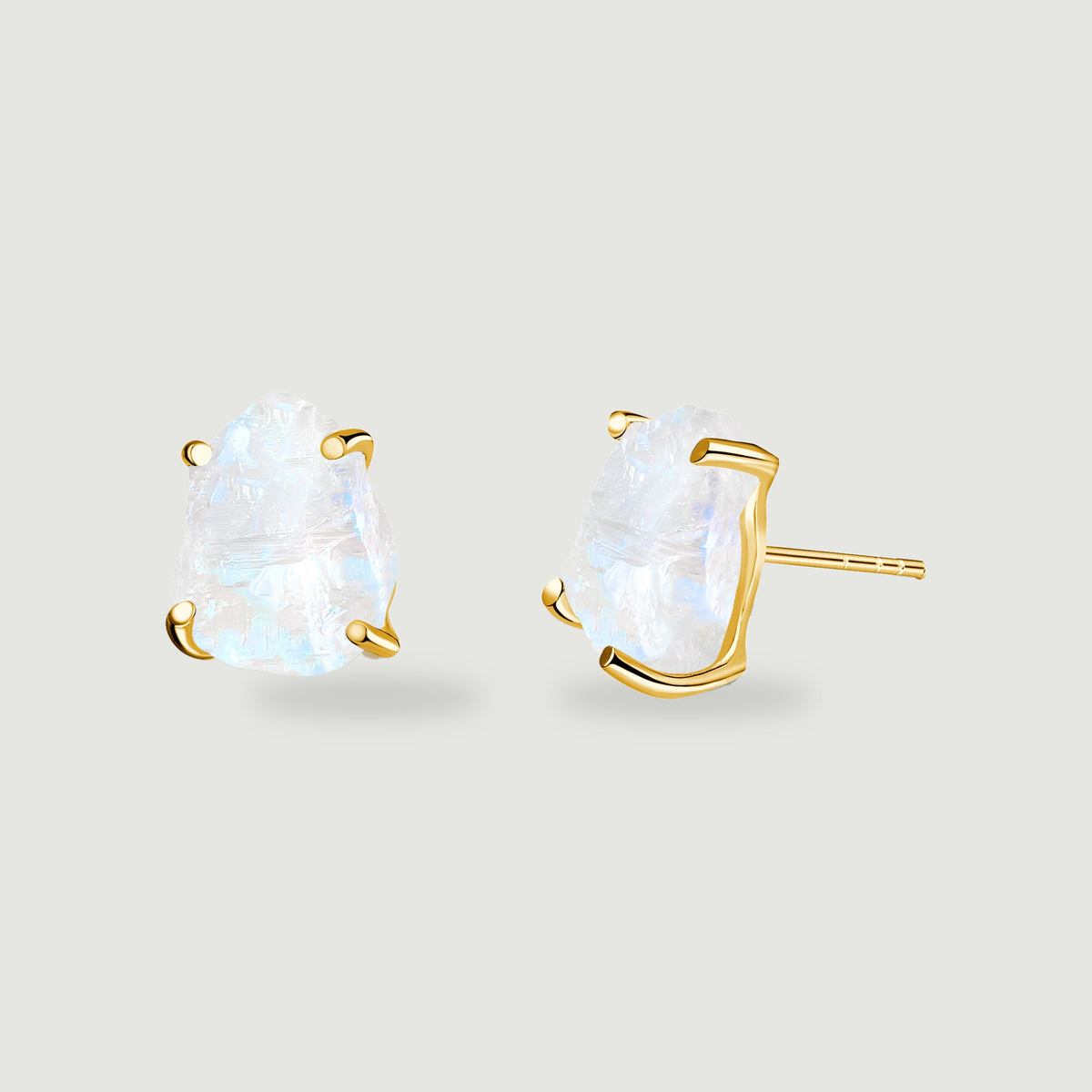A pair of raw moonstone earrings shows yellow gold prongs and a straight stud post against light gray.