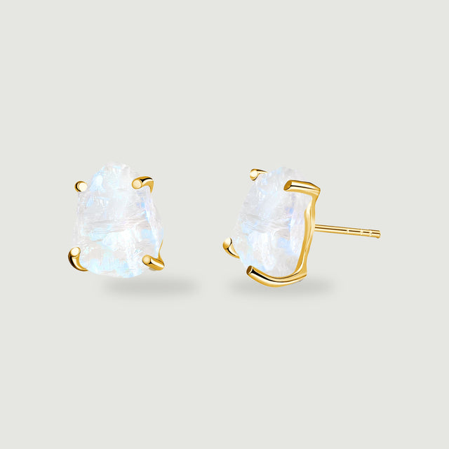 A pair of raw moonstone earrings shows yellow gold prongs and a straight stud post against light gray.