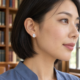A yellow gold moonstone stud is visible below a black bob haircut with library shelves behind.