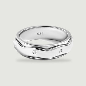 A sterling silver ring with wavy polished edges and three visible round white stones rests on a light gray surface.