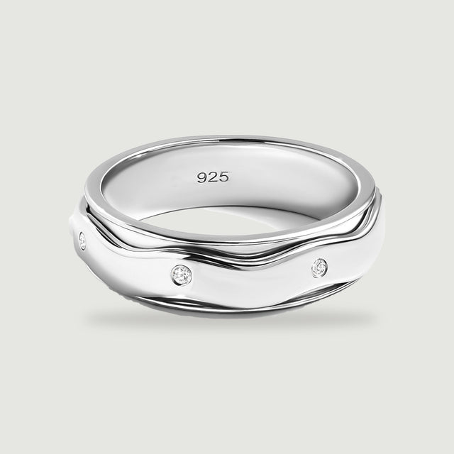 A sterling silver ring with wavy polished edges and three visible round white stones rests on a light gray surface.