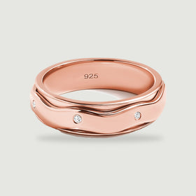 A rose gold vermeil ring displays curved polished rails and flush set white stones on a pale gray surface.