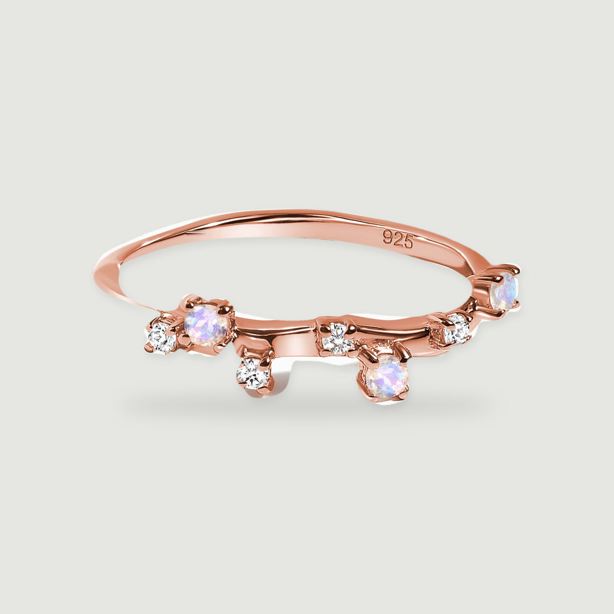 A rose gold vermeil ring has a slender polished band with blue-white stones and smaller clear accents.