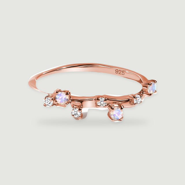 A rose gold vermeil ring has a slender polished band with blue-white stones and smaller clear accents.