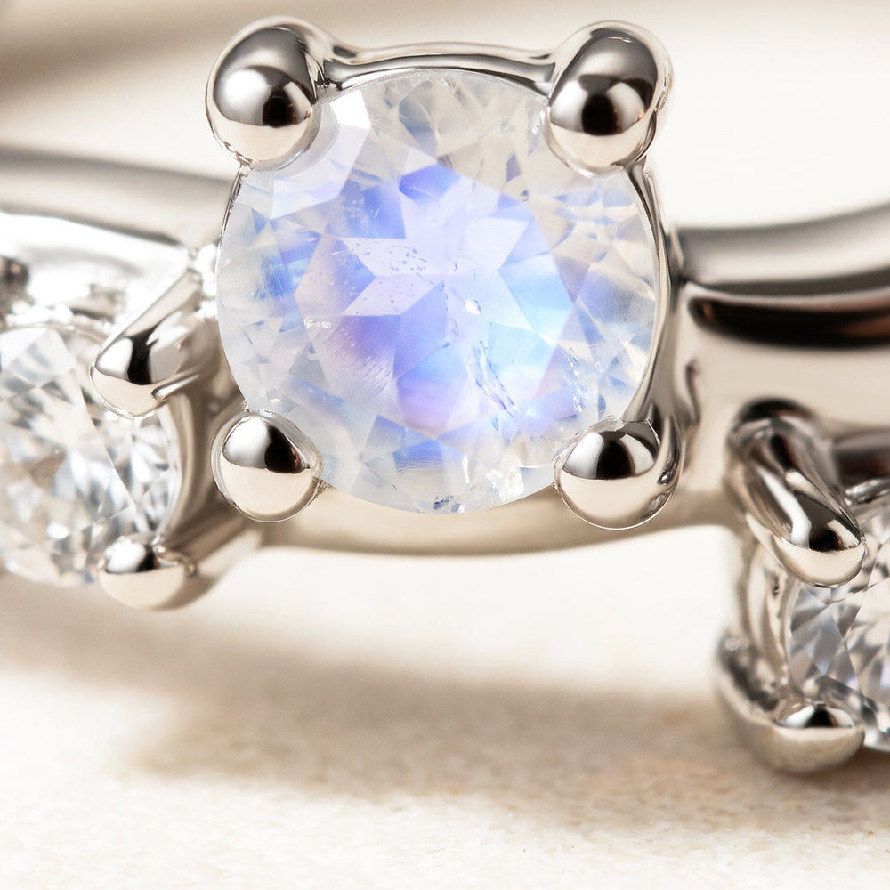 A close view shows a blue-white faceted stone held by rounded silver prongs beside smaller clear stones.
