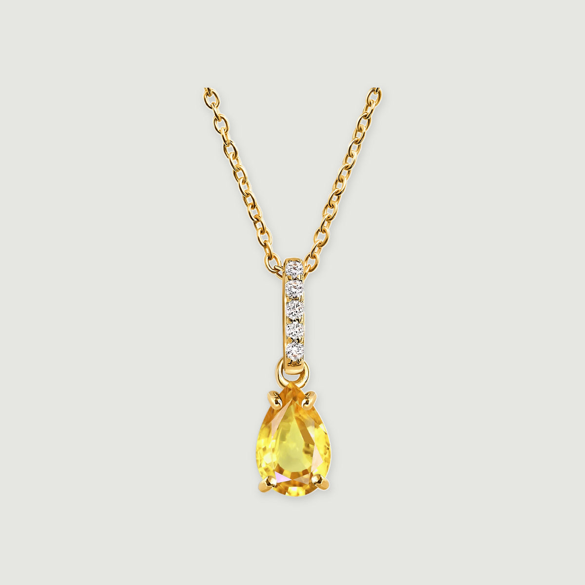 A pear-shaped yellow citrine hangs beneath a bar of five clear stones on a gold-toned chain against a light gray background.