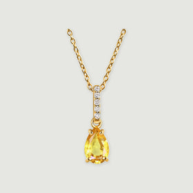 A pear-shaped yellow citrine hangs beneath a bar of five clear stones on a gold-toned chain against a light gray background.