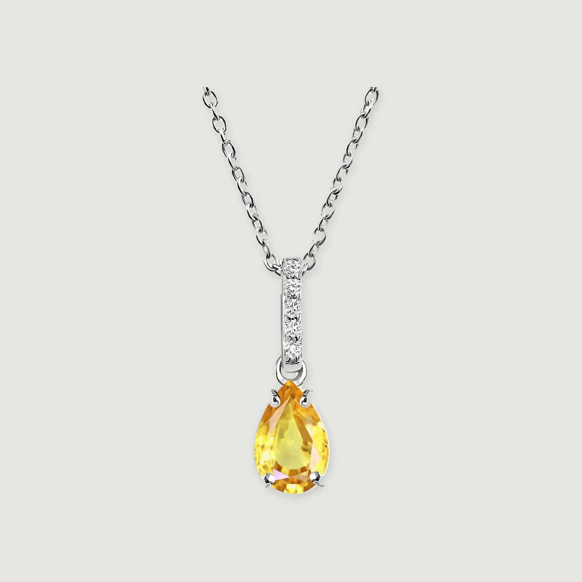 A silver-toned chain holds a yellow pear-shaped gemstone below a slim clear-stone bar on a pale gray surface.