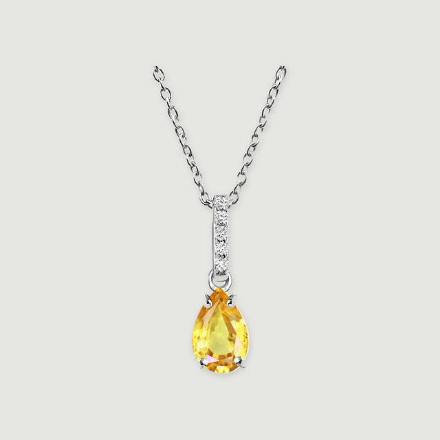 A silver-toned chain holds a yellow pear-shaped gemstone below a slim clear-stone bar on a pale gray surface.