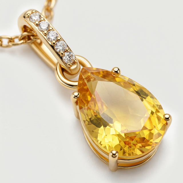 A close view shows the gold-toned prongs, yellow citrine facets, and five clear stones along the elongated bail.