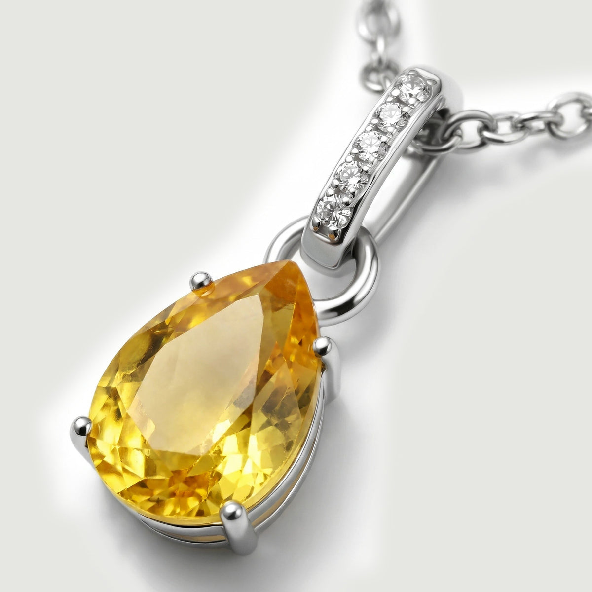 The angled silver pendant reveals rounded prongs around a faceted yellow stone and clear stones set into the bail.
